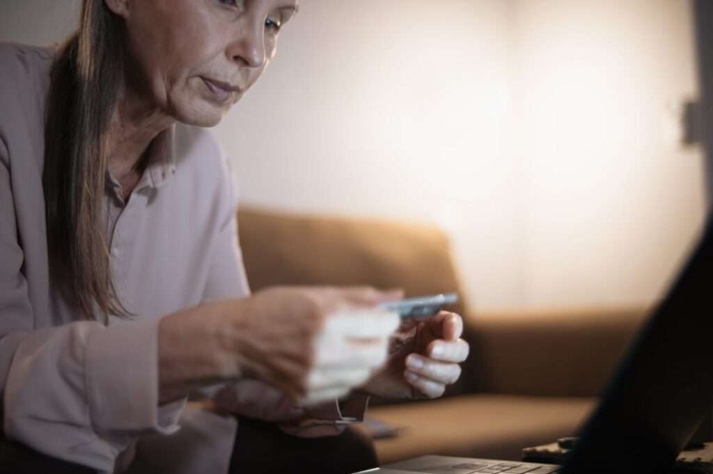 mulher idosa frente a tela segura cartao de credito na mao