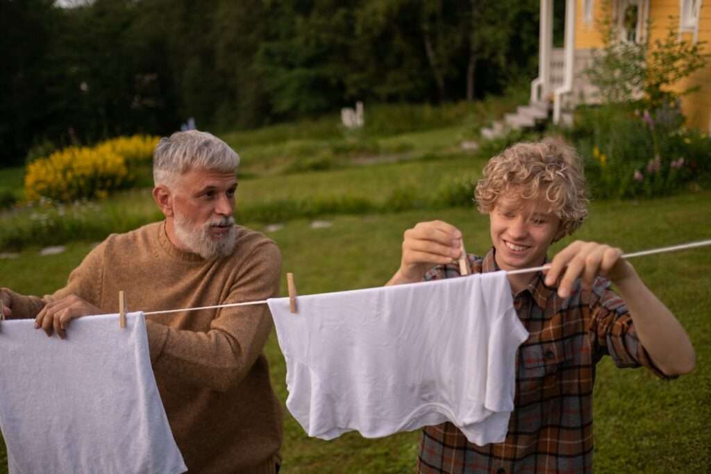 idoso de barba branca e adolescente penduram roupa no varal.