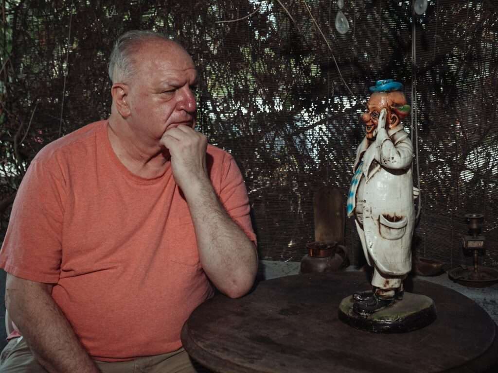idoso de perfil, triste olhando um a estatueta de palhaço