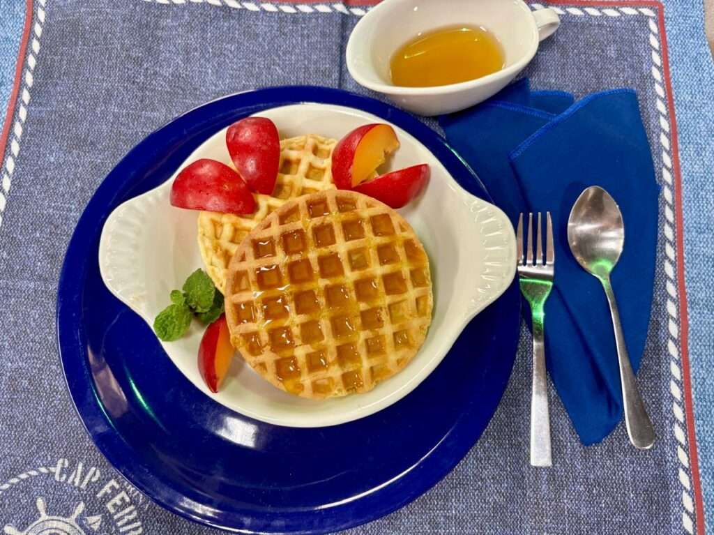 Um prato sobre a mesa contendo waffle com morangos em pedaços