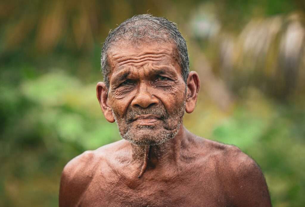 idoso sem camisa com fundo de mata olha para a camara
