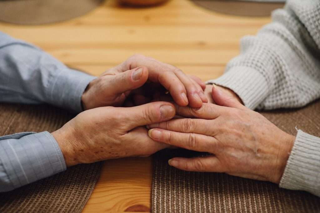 Mãos de duas pessoas idosas sobre uma mesa de madeira