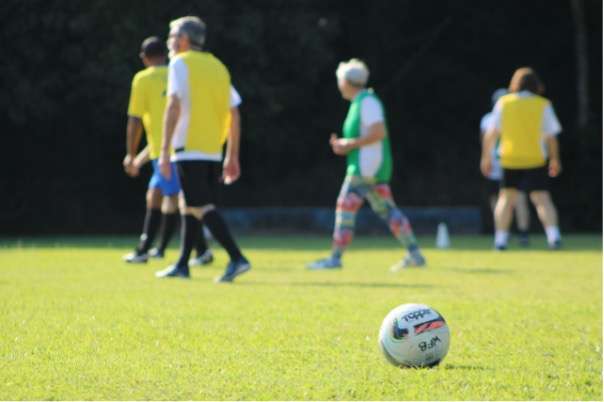 pessoas idosas caminham em um gramado tendo a bola como foco