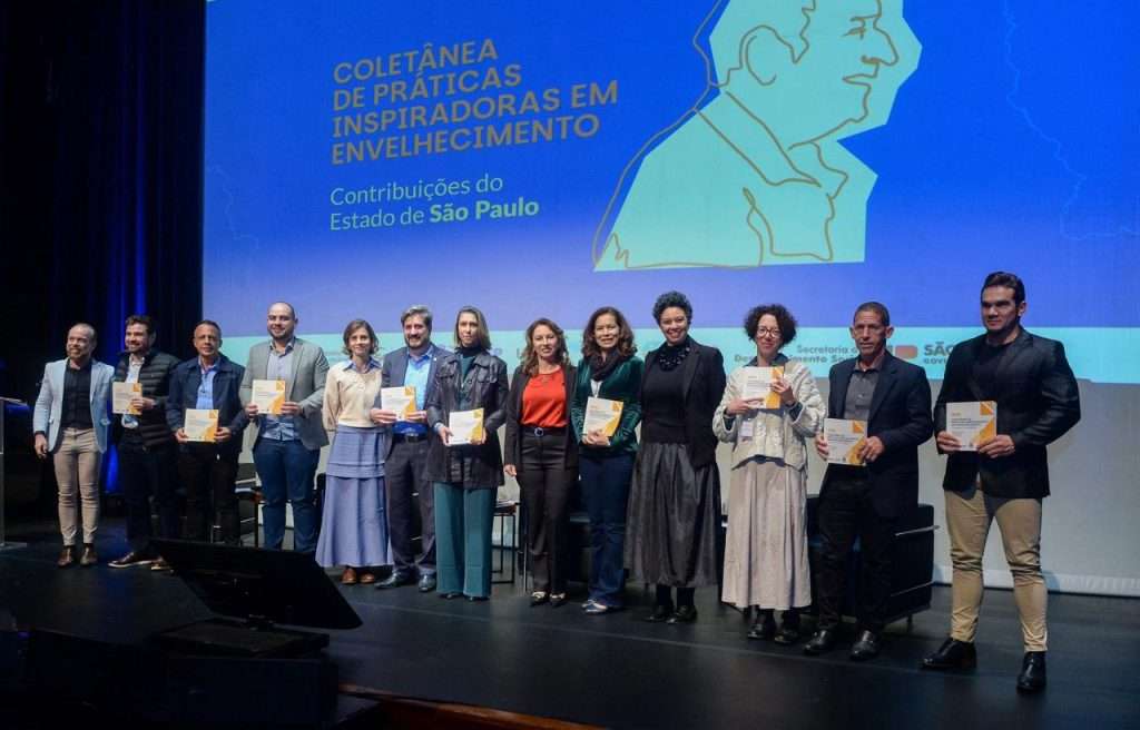 várias pessoas posam para foto mostrando em suas mãos a Coletânea de práticas que inspiram em envelhecimento