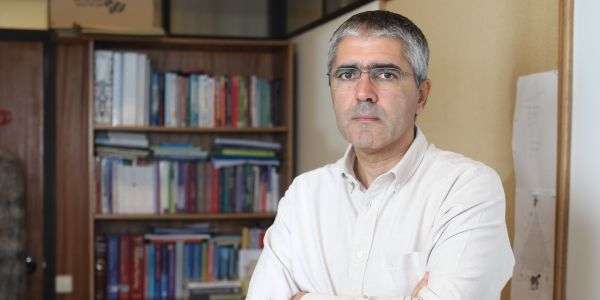Homem com camisa branca, de óculos, à frente de uma estante de livros.