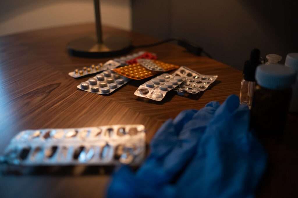 diversas cartelas de medicamentos em cima de uma mesa de cabeceira com luz noturna.