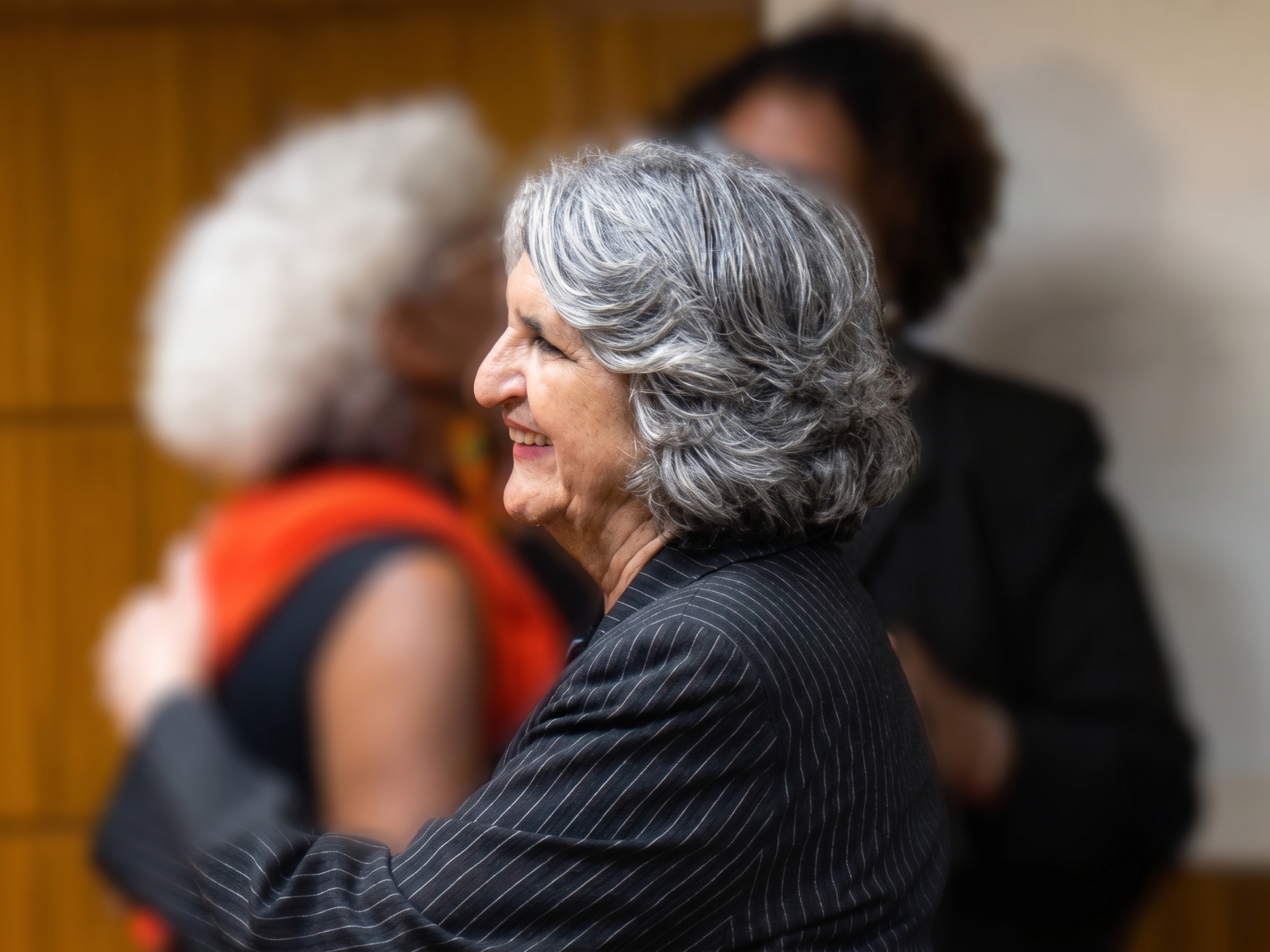Foto de Maria do Carmo Guido abraçando pessoas desfocadas